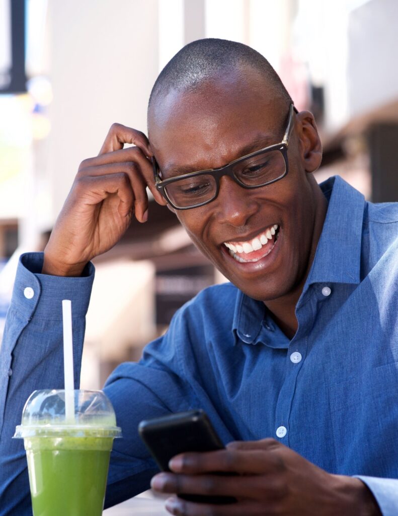 Black Man looking at phone with glasses on and a blue shirt with a green smoothy