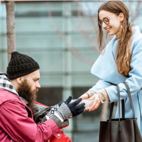 Lady in blue coat giving to a homeless man in a red coat